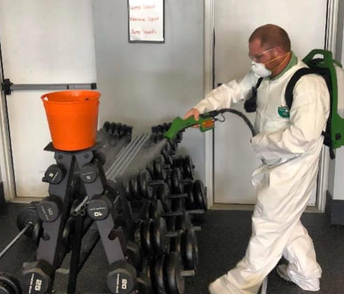 man in personal protective equipment spraying disinfectant 